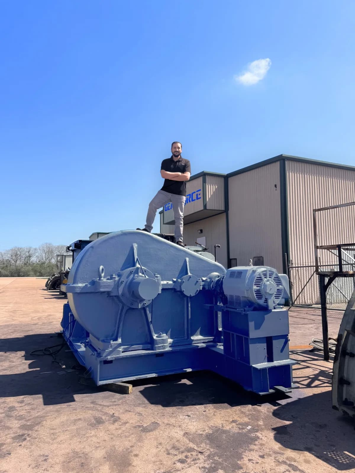A Gear Force Machine team member standing atop a large, freshly rebuilt blue industrial gearbox outside the Rosharon, Texas shop — a sense of the scale of the units we rebuild.