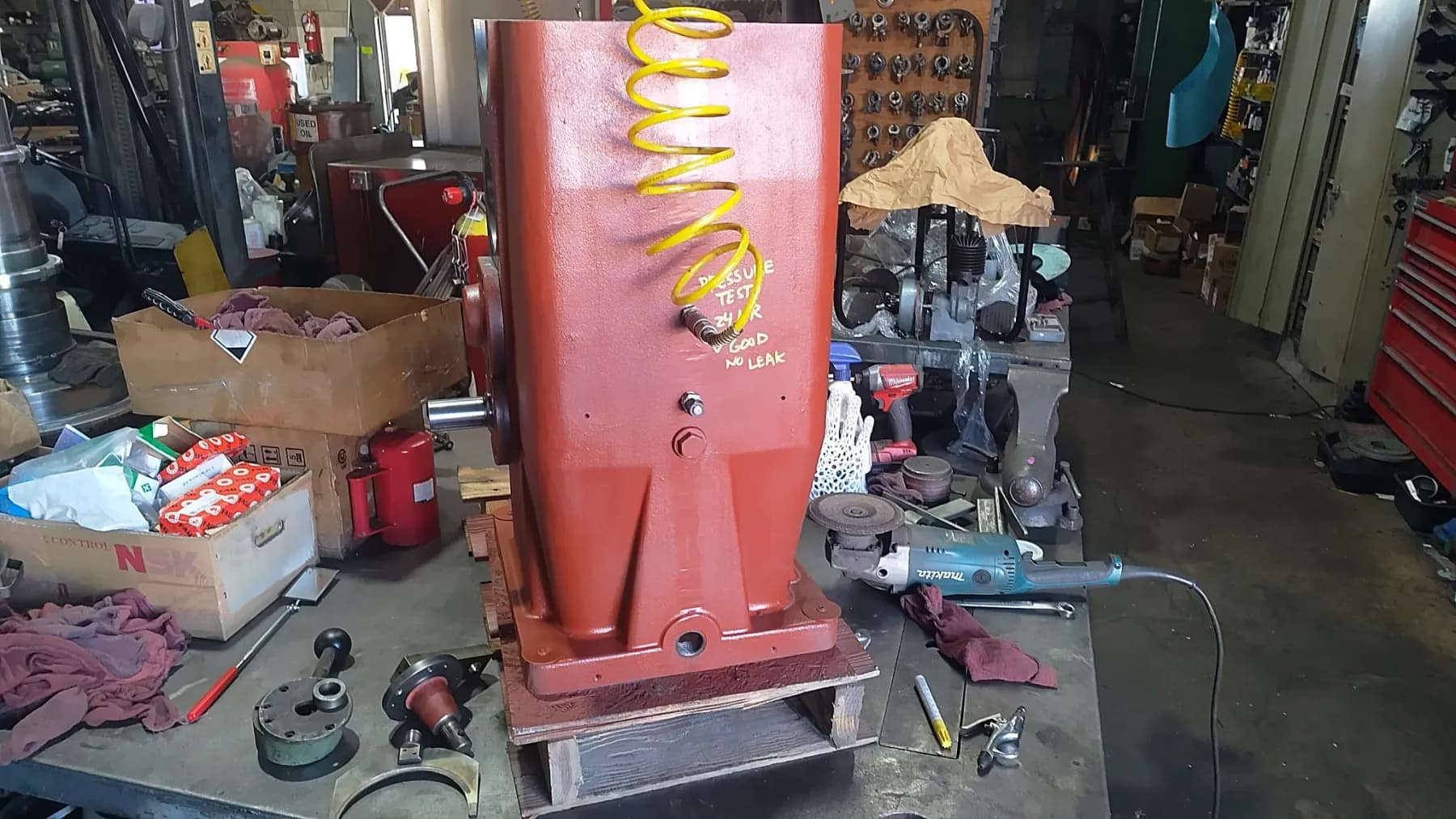 A rebuilt red industrial gearbox pressure-tested and tagged 'GOOD — NO LEAK', staged for emergency return to service.